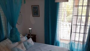 Et soveværelse med en seng, et natbord, en lampe og et vindue med gardiner.