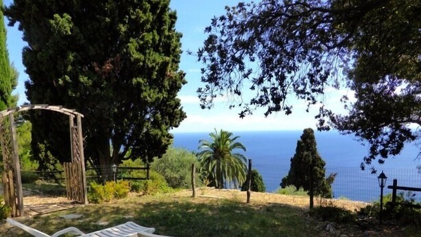 A garden with two white lounge chairs, a wooden pergola, and a view of the sea.