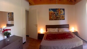 A bedroom with a bed, bedside lamps, a painting on the wall, and a door leading to another room.