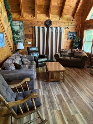Relax in this inviting living room with a leather armchair, sofa, and wooden rocking chair, surrounded by a wooden coffee table and framed artwork.
