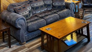 Ein gemütliches Blockhaus-Interieur mit einer Holztreppe, einer Couch mit Tier-Kissen, einem Holztisch und einem gerahmten Bild an der Wand.