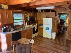 Kitchen with stove, sink, and refrigerator, featuring a central island and window with outdoor view.