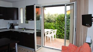 A compact kitchen with dark cabinets, a dining area with a table and chairs, and a sliding glass door leading to a patio with a view of greenery. - Quiet 500 m from Lozari beach (Palasca)