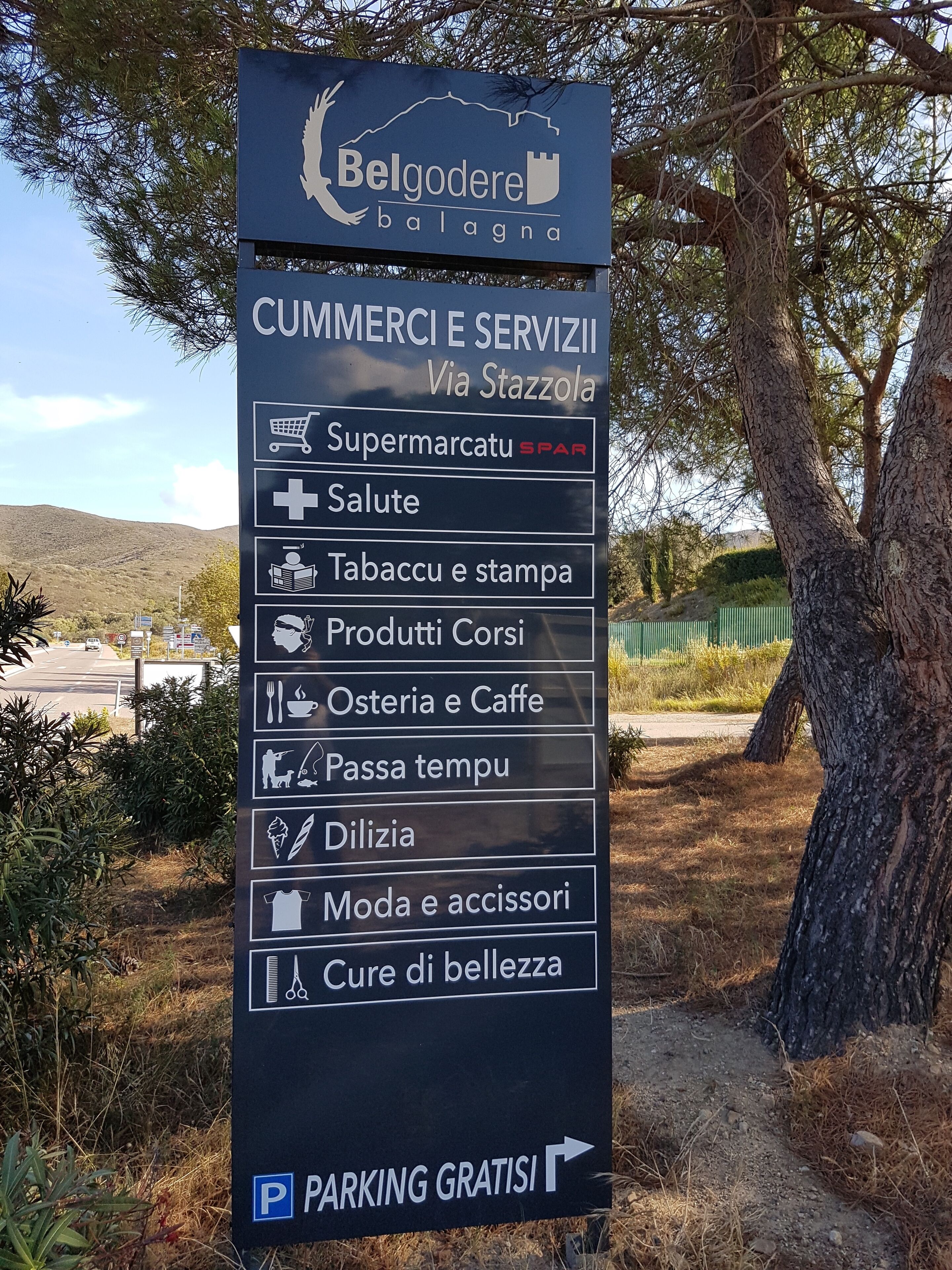 A sign for 'Belgodere balagna' with a list of services including a supermarket, pharmacy, tobacco, coffee, and beauty salon.