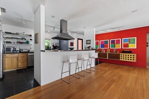 Una cocina moderna con una isla central, taburetes de bar y una pared roja decorativa.