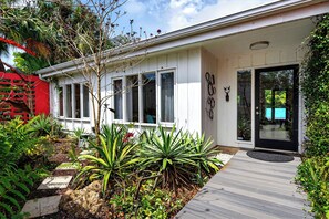 Una casa moderna con terraza de madera, ventanas amplias y un jardín con plantas tropicales.
