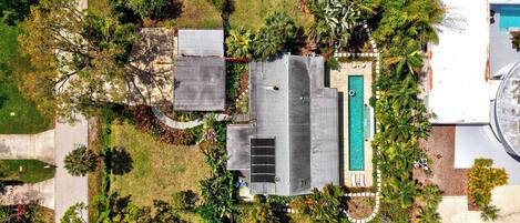 Vista aérea de una propiedad residencial con piscina, paneles solares y jardín.