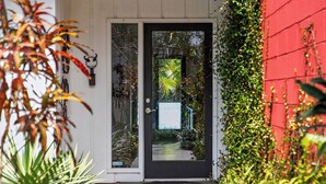 A modern house with a black door, a small porch, and a red wall covered in greenery. - Mid-Century Modern W/Private Lap Pool In secluded Garden and art studio (Sarasota)