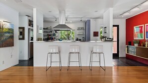 A modern kitchen with a central island, bar stools, and a red accent wall. - Mid-Century Modern W/Private Lap Pool In secluded Garden and art studio (Sarasota)