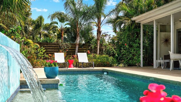 A pool with a waterfall feature, surrounded by lush greenery and palm trees. - Mid-Century Modern W/Private Lap Pool In secluded Garden and art studio (Sarasota)