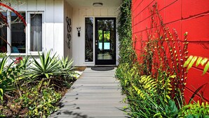 A modern house with a red wall, a white exterior, and a wooden pathway leading to a black door. - Mid-Century Modern W/Private Lap Pool In secluded Garden and art studio (Sarasota)