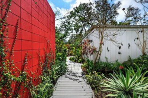 Un sendero estrecho bordeado por exuberante vegetación y un muro rojo.