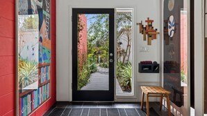 A hallway with a door leading to a garden, a wooden bench, and a wall with artwork and a clock. - Mid-Century Modern W/Private Lap Pool In secluded Garden and art studio (Sarasota)