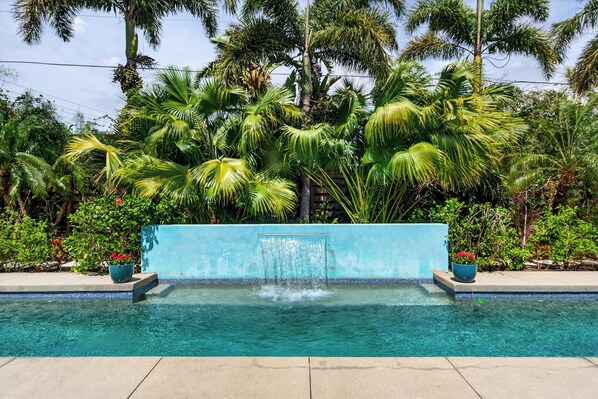 Una piscina con caída de agua, rodeada de exuberante vegetación tropical.