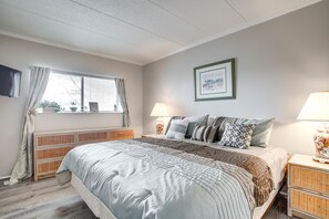 Ein Schlafzimmer mit einem großen Bett, zwei Nachttischen mit Lampen, einem Fenster mit Vorhängen, einem gerahmten Bild an der Wand und einem Korbuscheinheit.