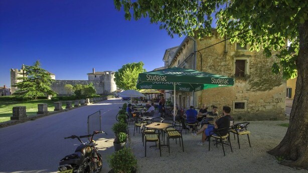 An outdoor cafe with tables and chairs, a motorcycle parked nearby, and a stone building in the background. - Countryside Holiday Apartment In Village Peresiji (Peresiji)
