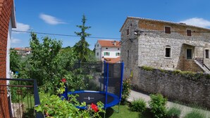 A stone building with a red-tiled roof, a blue trampoline in a fenced yard, and a brick wall. - Countryside Holiday Apartment In Village Peresiji (Peresiji)