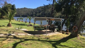A covered picnic area with a grill, seating, and a view of a lake. - Hawkesbury River Guest House (Lower Portland)