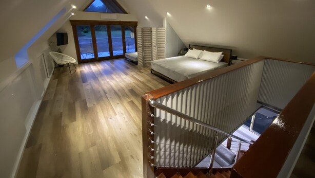 A bedroom with a sloped ceiling, a bed, a chair, and a view of the outside. - Hawkesbury River Guest House (Lower Portland)