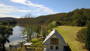 A house with a sloped roof, a lawn, and a lake in the background. - Hawkesbury River Guest House (Lower Portland)