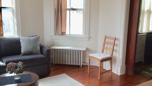 Een woonkamer met een bank, een houten stoel, een salontafel en een radiator.