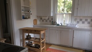 Een keuken met witte kastjes, een houten tafel met pannen en potten, een raam met gordijnen en een betegelde achterwand.