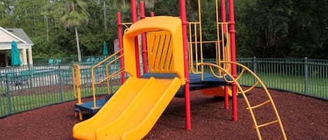 A playground with a yellow slide and red and yellow play structures.