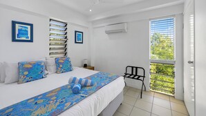 Ein Schlafzimmer mit Bett, Kissen, einem Fenster mit Jalousien, einem Deckenventilator und einer Klimaanlage.