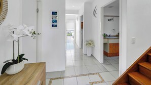 Ein moderner Flur mit weißen Wänden, einem hölzernen Empfangsbereich und einer Treppe zu einem Küchenbereich.