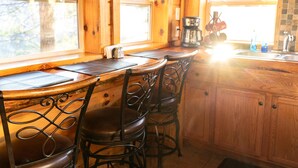 A wooden bar with three metal chairs, a coffee maker, and a sink with a faucet. - Bear Lair: Luxe cabin, private lake, caves, trails, fast WiFi @ Bear Track Lake (Beattyville)