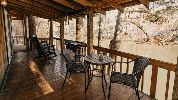 A wooden deck with a table and chairs overlooking a body of water, surrounded by trees. - Bear Lair: Luxe cabin, private lake, caves, trails, fast WiFi @ Bear Track Lake (Beattyville)