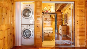 A wooden cabin interior with a washing machine, a bed, and a small kitchenette. - Bear Lair: Luxe cabin, private lake, caves, trails, fast WiFi @ Bear Track Lake (Beattyville)