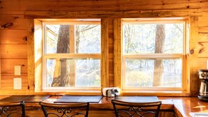 A wooden cabin interior with two large windows, a wooden table, and metal chairs. - Bear Lair: Luxe cabin, private lake, caves, trails, fast WiFi @ Bear Track Lake (Beattyville)