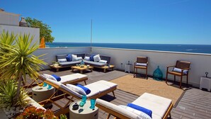 Un espace de détente extérieur baigné de soleil, avec des fauteuils et des canapés confortables, une terrasse en bois et une vue sur la mer.