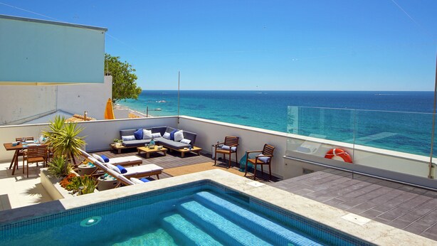 Un espace piscine aménagé sur le toit, avec des chaises longues, une petite table et une vue sur la mer.