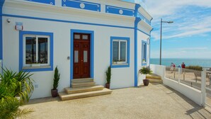 Un bâtiment à la façade bleue et blanche, avec une porte en bois et des plantes en pot.