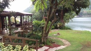 Un belvédère en bois doté d’une terrasse donnant sur un lac, entouré d ’une végétation luxuriante et bordé d’un sentier en pierre.