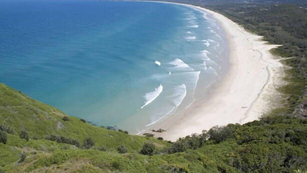 A coastal landscape with a long sandy beach and a clear blue ocean.