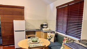 A compact kitchen with a refrigerator, a sink, and a countertop. There is a dining table with chairs and a bench with cushions.