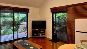 A spacious living room with large sliding glass doors, a ceiling fan, a flat-screen TV, and a wooden coffee table.