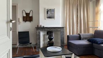 A living room with a sofa, a coffee table, a fireplace, and a door.
