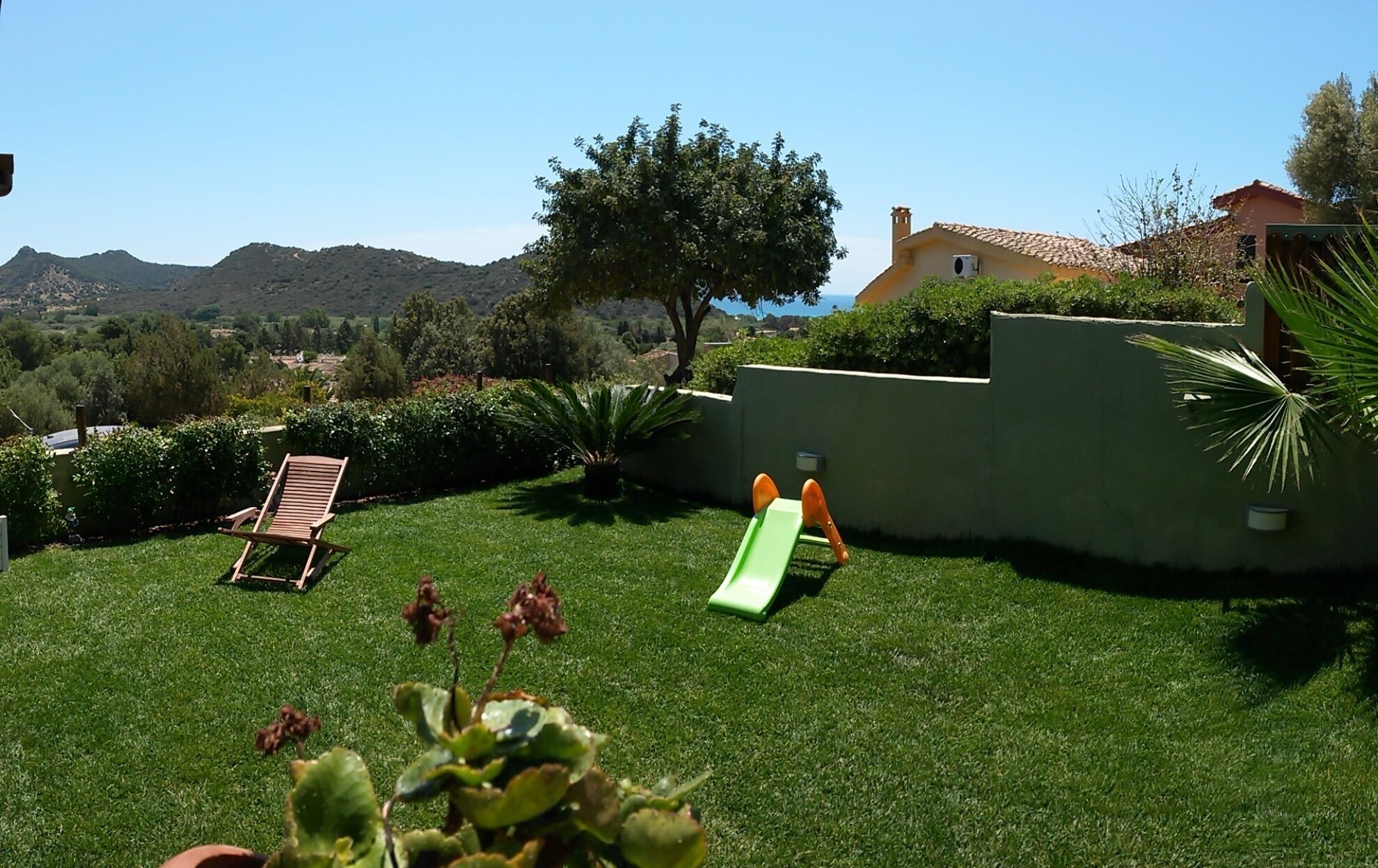 Un patio trasero con césped verde, una silla de madera, un tobogán verde y un árbol.