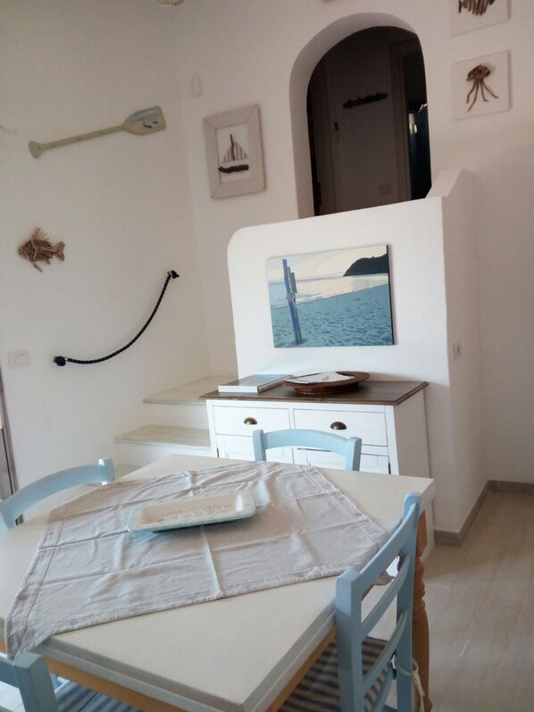 Un coin repas avec une table dressée pour deux personnes, un meuble blanc et un tableau représentant une scène de plage.