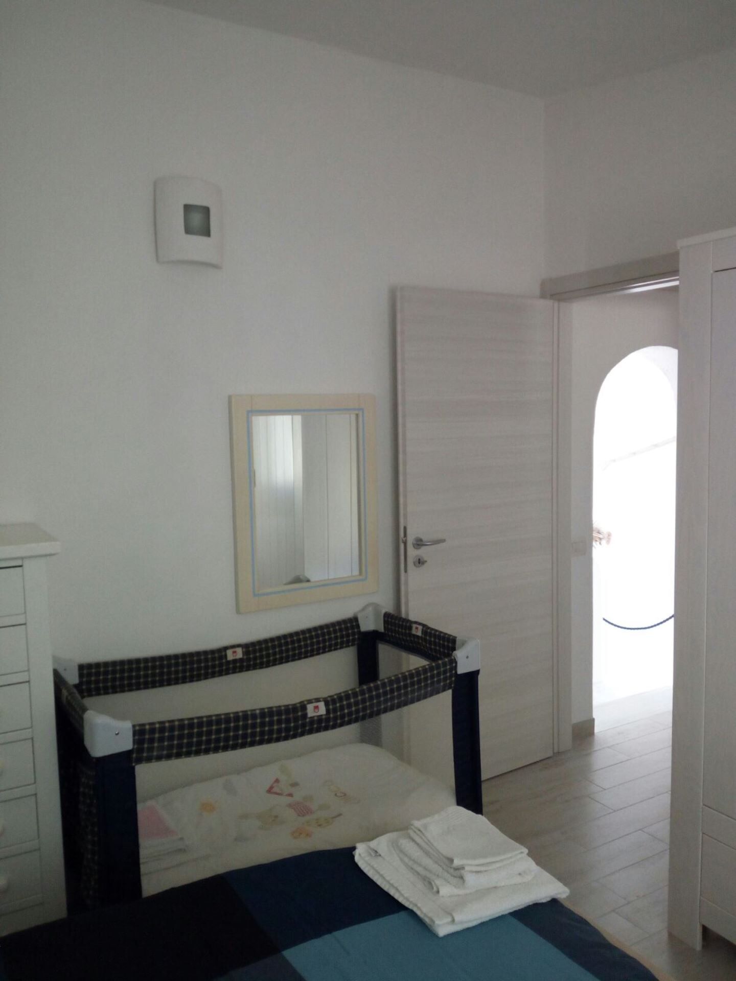 Una camera da letto con un letto, un comodino, uno specchio, una porta e vista sull'esterno.