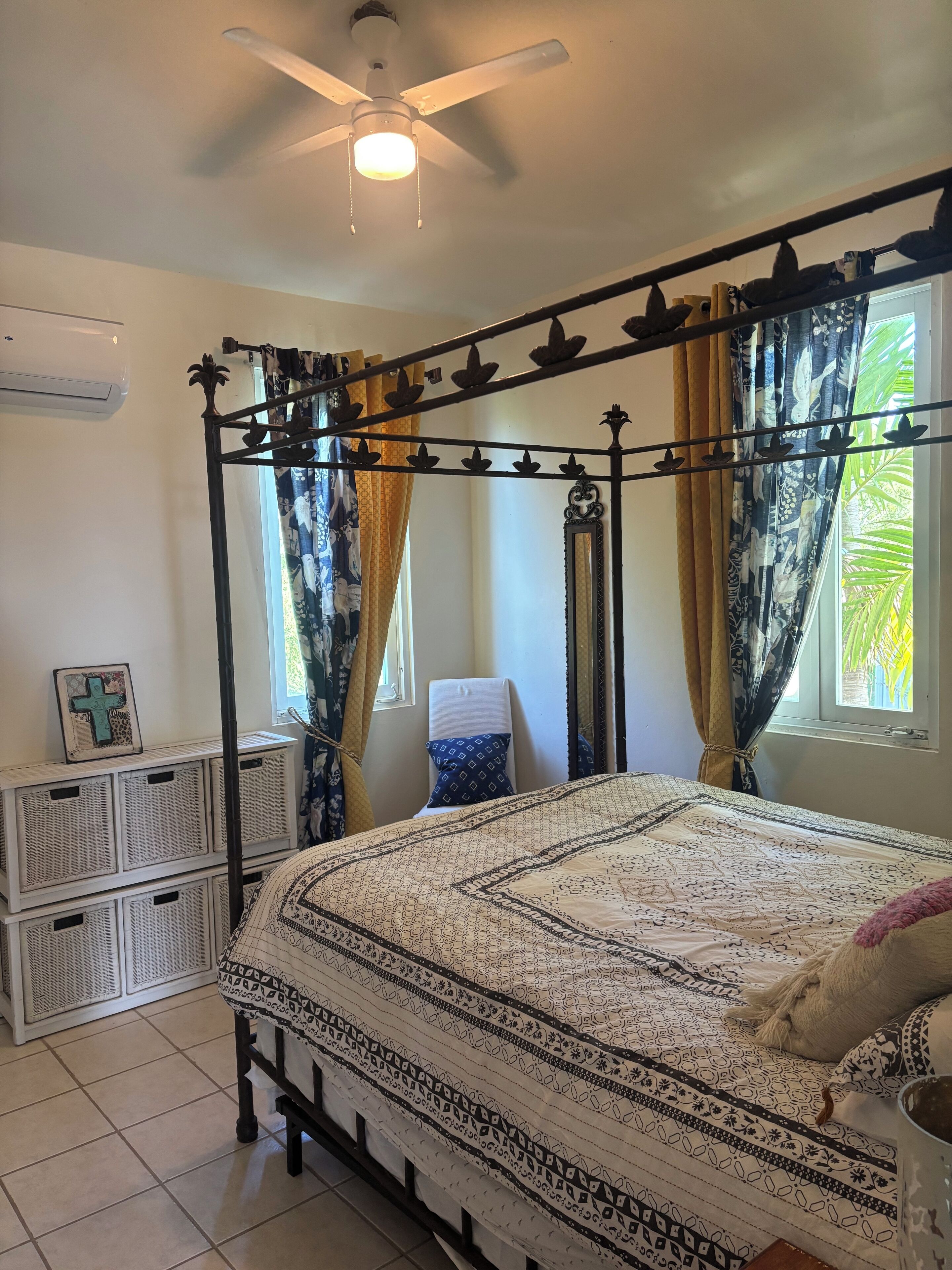 A bedroom with a four-poster bed, a ceiling fan, and a window with curtains.