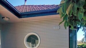 Una casa con un patio empedrado, un pequeño jardín con flores rosas y un ventanal circular.