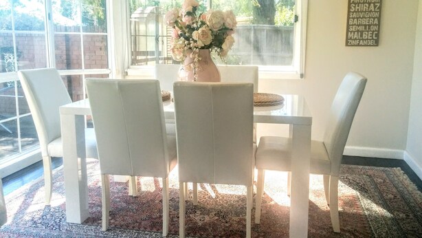 Un comedor con una mesa y sillas blancas, un jarrón de flores y una pared con una lista de tipos de vino.