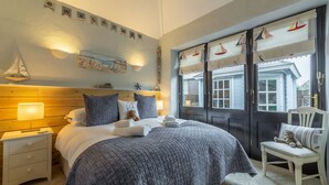 Quarto bem arrumado com cama, mesas de cabeceira, uma cadeira e uma janela com cortinas.