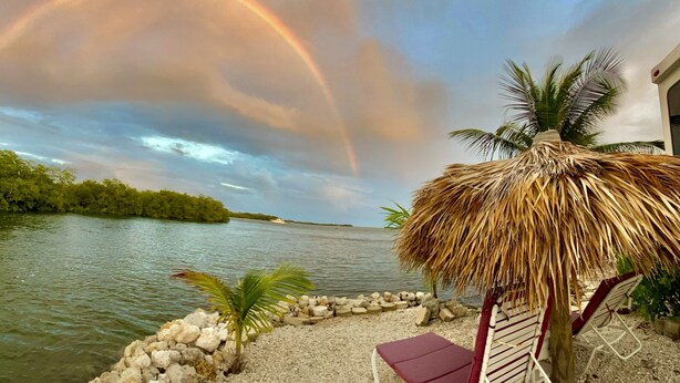 A beachside view with a thatched umbrella, a lounge chair, and a rocky shoreline. - Ocean Front with Dock, Key Largo, FL., Pirate's Cove (Key Largo)