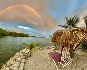 A beachside view with a thatched umbrella, a lounge chair, and a rocky shoreline. - Ocean Front with Dock, Key Largo, FL., Pirate's Cove (Key Largo)